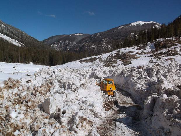 Glenn Schryver's bulldozer is dwarfed by the snowfield along Lincoln Creek Road. Bashing through tree trunks and boulders forced emergency repairs on the machine.